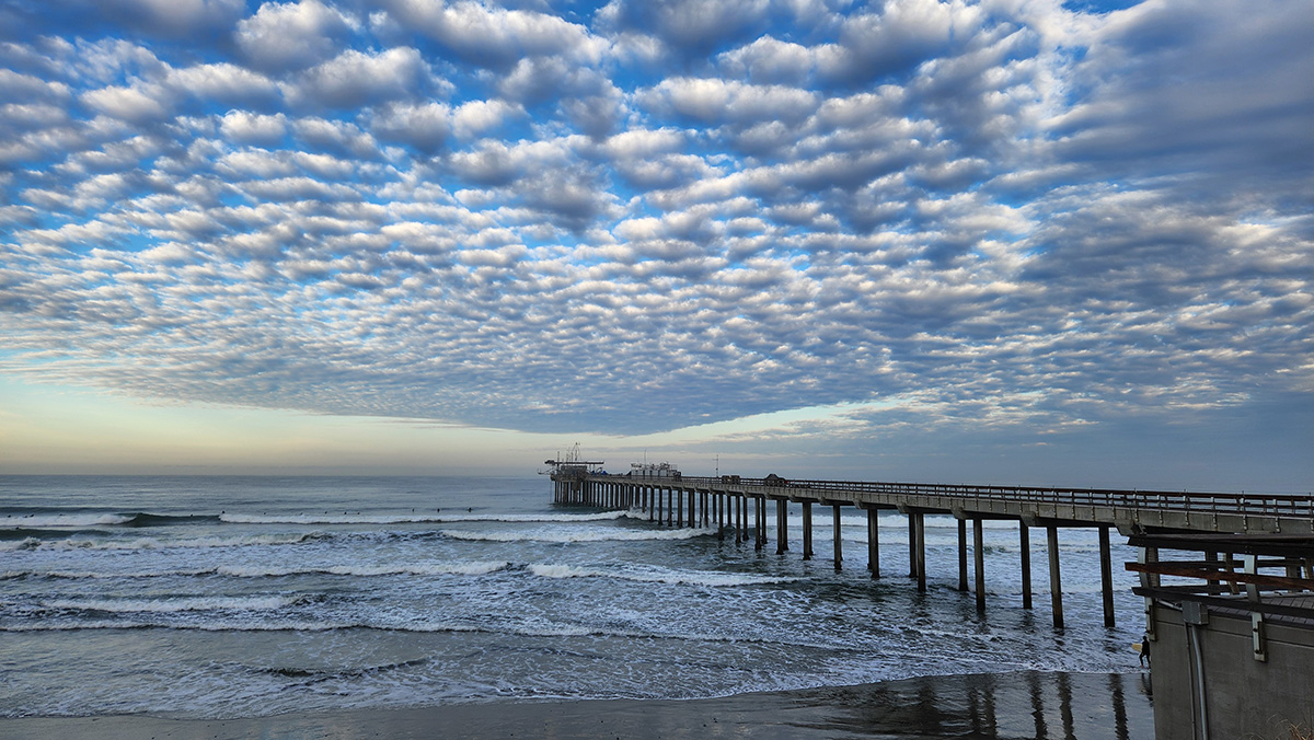 The restless ocean and atmosphere around Scripps Pier is on full display in this January 2024 view. ARM containers and instruments are seen on the pier with puffy clouds overhead.