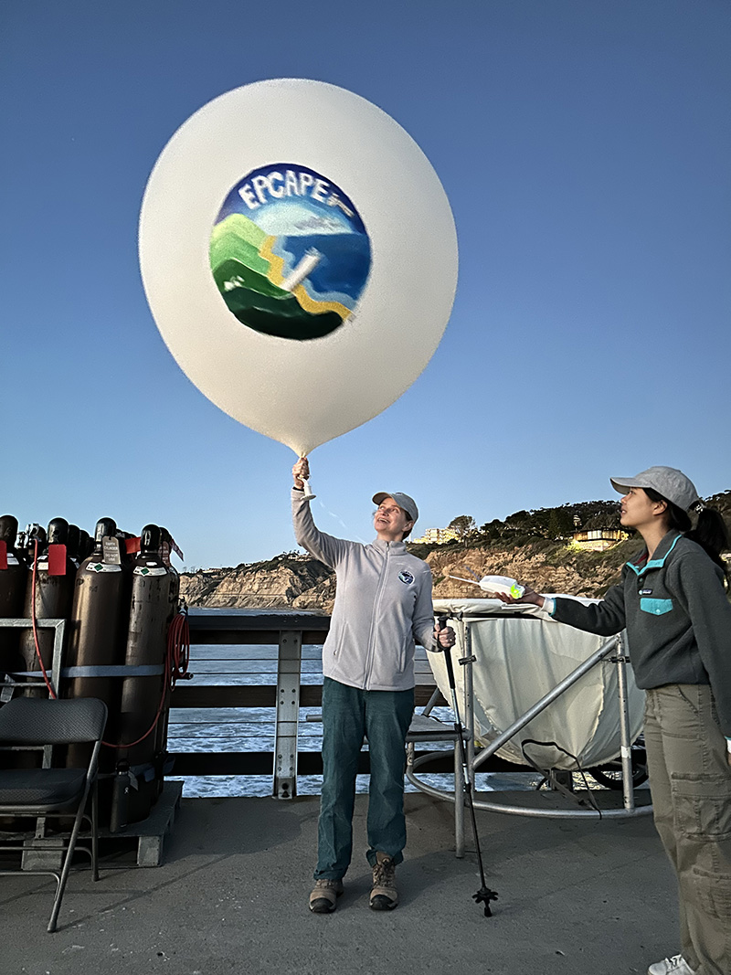 Lynn Russell, principal investigator of the yearlong Eastern Pacific Cloud Aerosol Precipitation Experiment (EPCAPE), launches the field campaign’s final radiosonde at 6 p.m. Pacific on February 14, 2024. The launch took place on the Ellen Browning Scripps Memorial Pier in La Jolla, California. A picture depicting EPCAPE is painted on the weather balloon attached to the sonde.