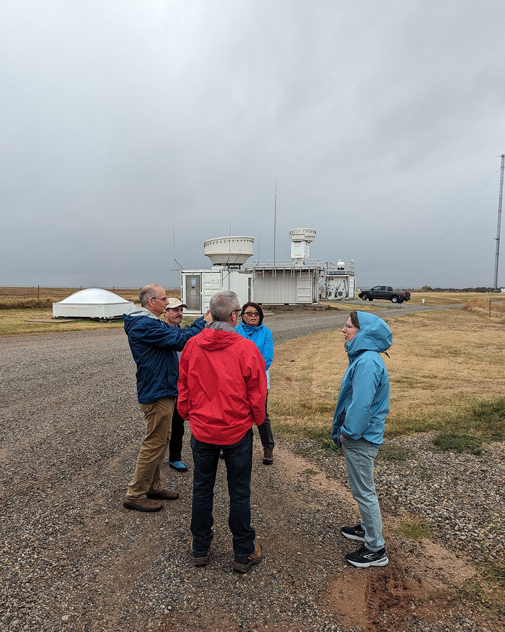 Jen Delamere talks with Mike Ritsche, Jim Mather, Connor Flynn, and Yunyan Zhang in front of ARM radars and lidars at the Southern Great Plains Central Facility.