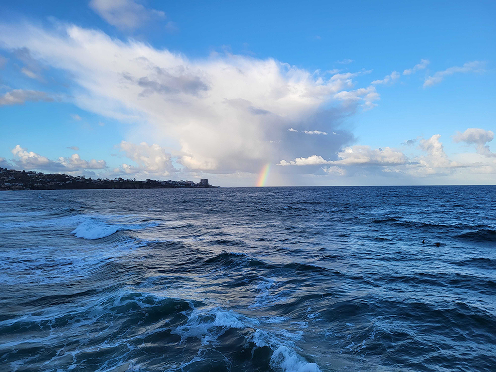 Waves are captured in motion while a rainbow is seen in the distance.