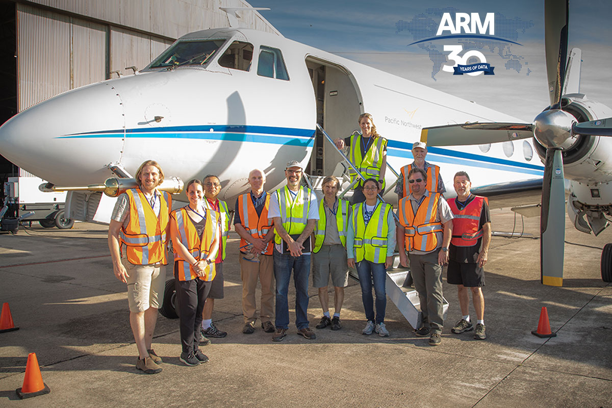 Crew members wearing bright orange and yellow safety vests gather on and around G-1 turboprop aircraft