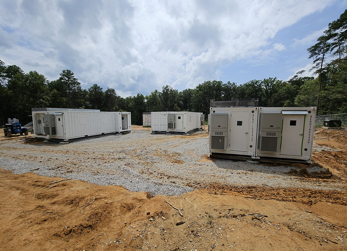 A cluster of sea containers sits on gravel in a forest clearing.