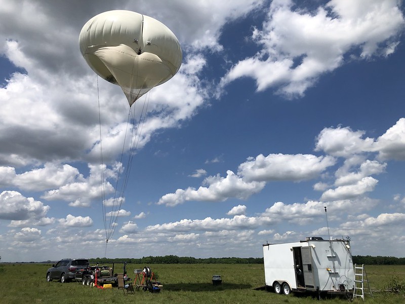 A tethered balloon system rises above the TRACER site in Guy, Texas. A trailer sits next to the van set up for the balloon flight.