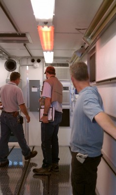 amf2-aos Left to right: Pat Maloy, Stephen Springston, and Mike Ritsche inspect the AMF2 AOS container. They checked for proper locations of unistrut on the ceiling, walls and floor for connecting racks and other equipment, as well as functioning of HVAC units and infrared heaters (above Mike's head). Red lights are required for nighttime ship operations, and the hatch in ceiling will accommodate the aerosol stack. ARM file photo.